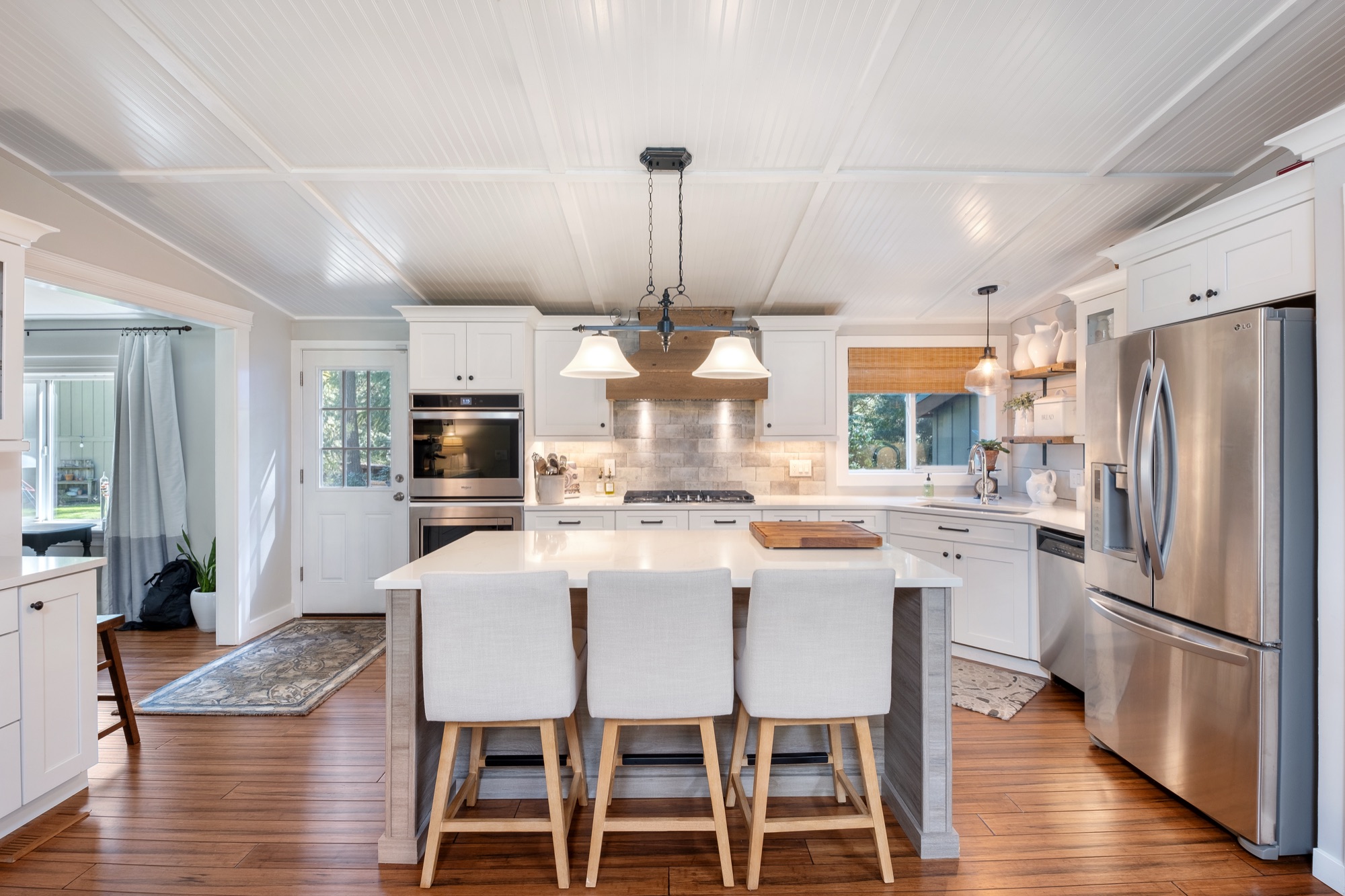 White kitchen with beadboard ceiling, stone backsplash, and stainless fridge