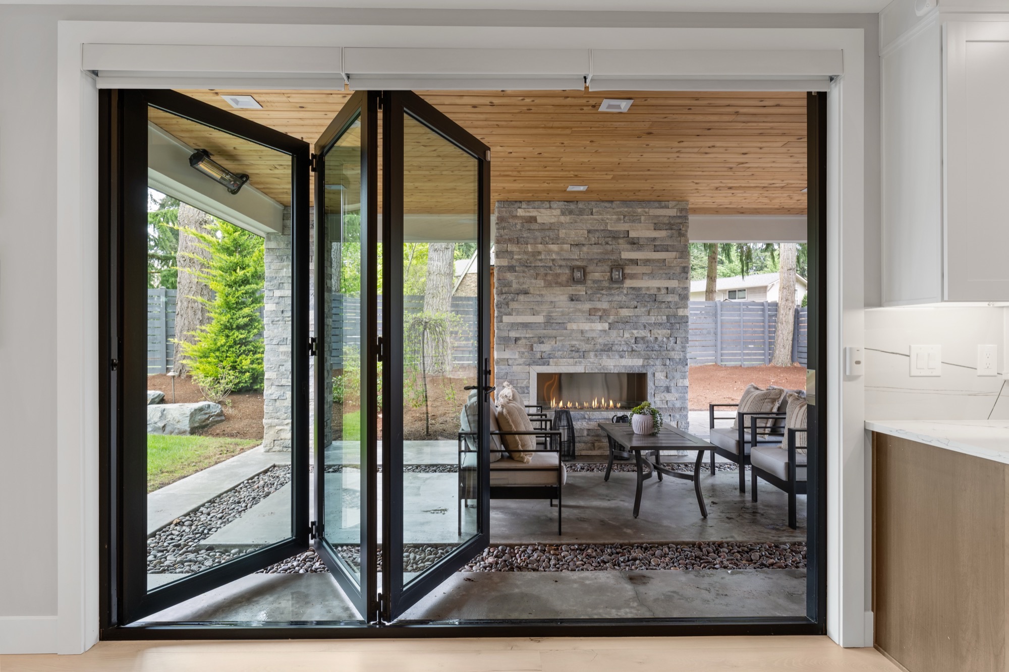 Folding glass doors opening to a covered patio with stone fireplace
